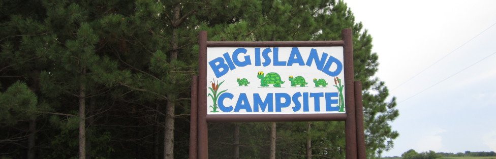 The Big Island Campsite sign, with its turtle logo, in front of tall pine trees