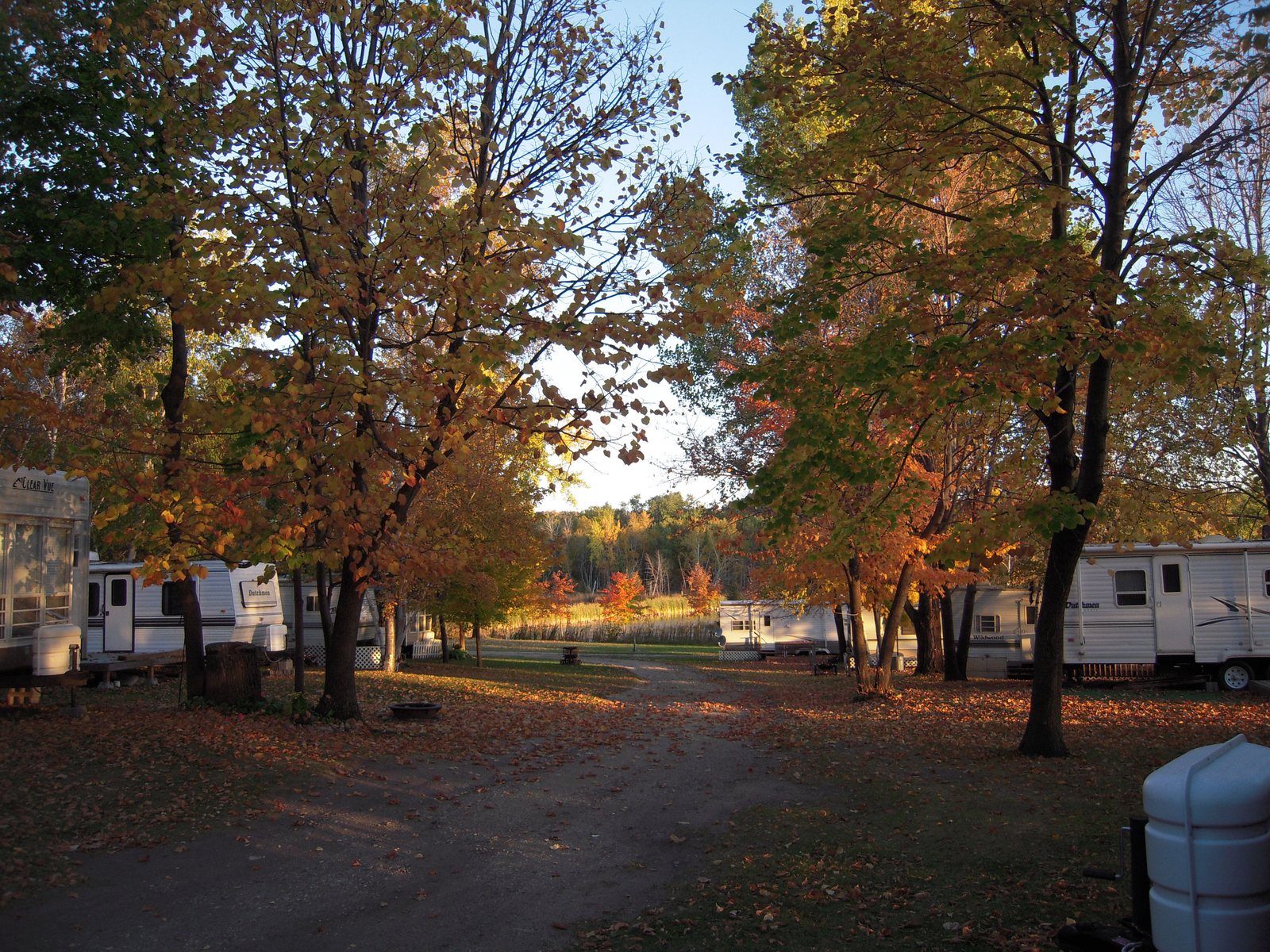 Seasonal trailers under autumn trees along the campground road, with the lake beyond